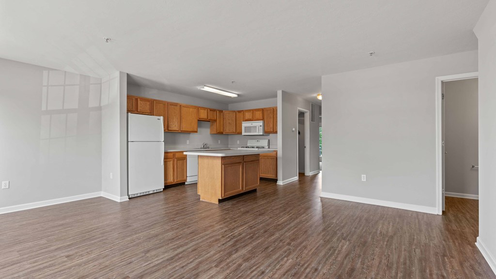 an empty living room with a kitchen with wood floors and white appliances