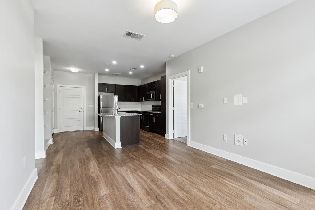 the living room and kitchen of an apartment with white walls and wood flooring