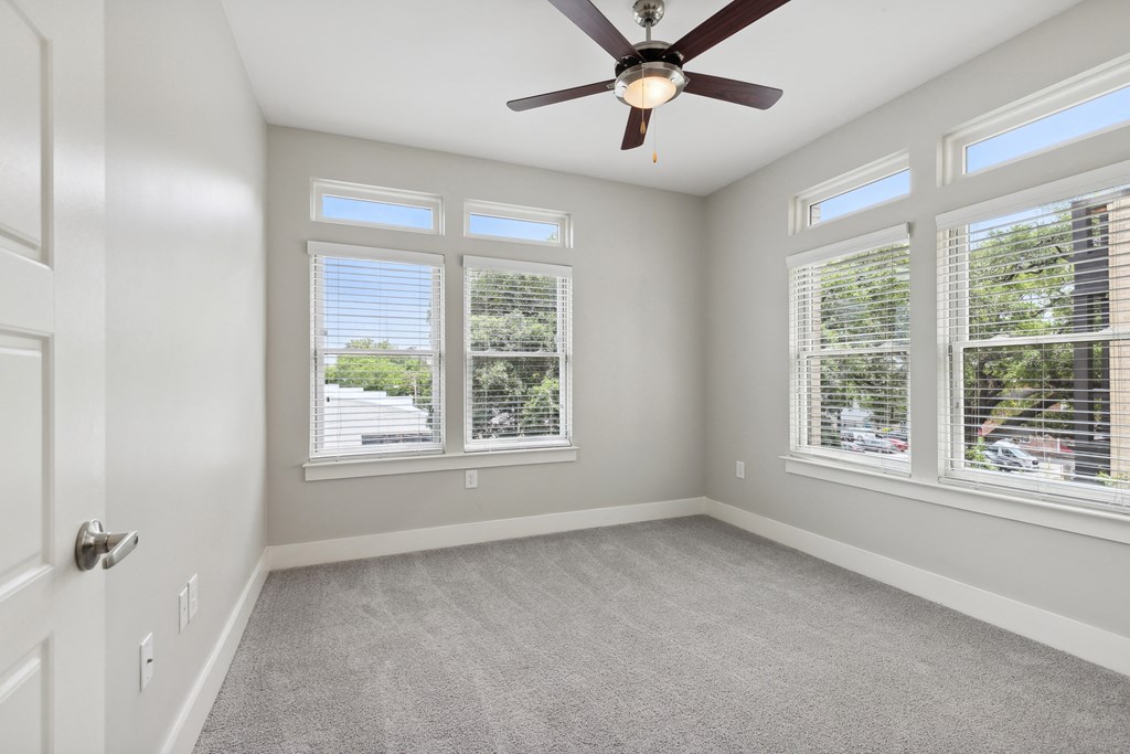 an empty bedroom with a ceiling fan and three windows
