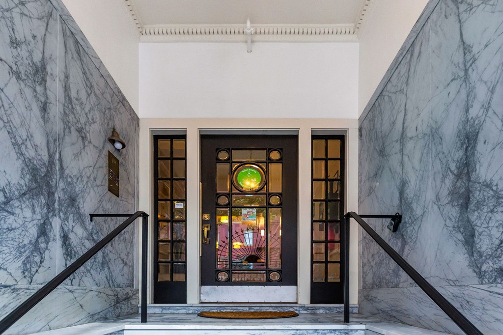 A white and grey marbled hallway with a black door and a small window.