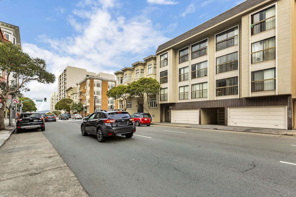 A black car is driving down a street lined with parked cars and buildings.