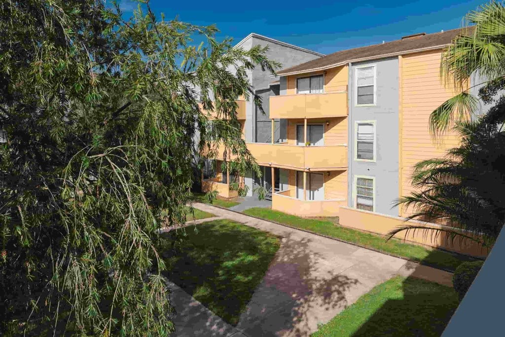 an apartment building with a driveway and trees in front of it