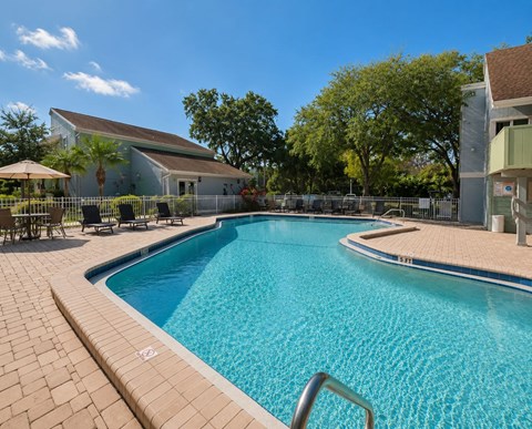 A swimming pool surrounded by a brick patio and a white building in the background.