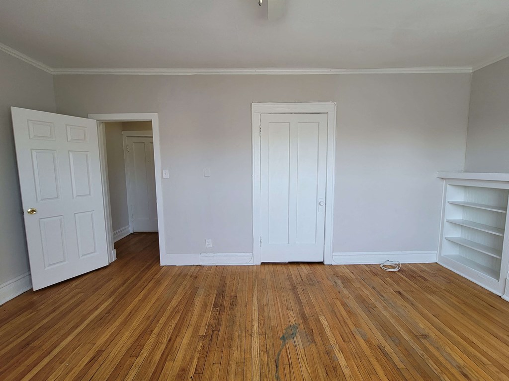 a bedroom with white walls and wooden floors and two closets