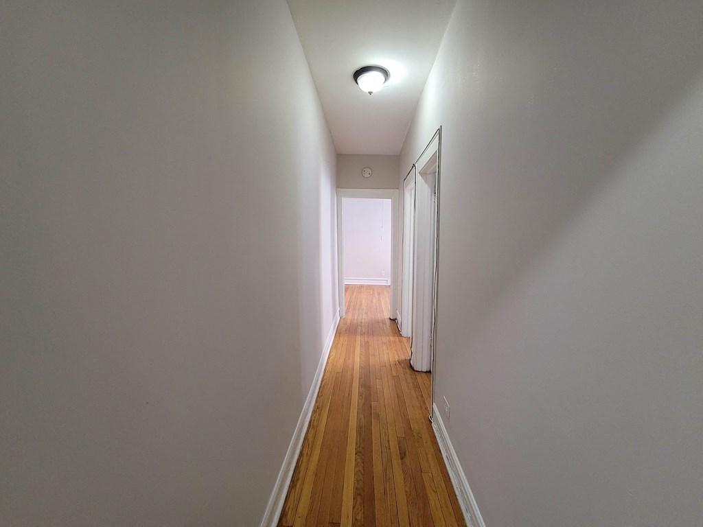 a long hallway with white walls and wooden floors and a light on the ceiling