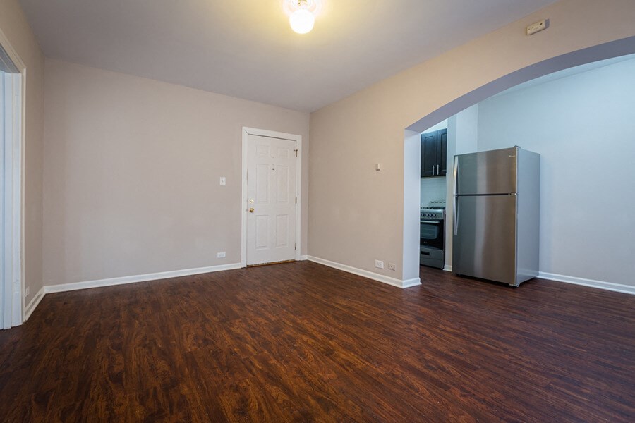 an empty living room with wood flooring and a refrigerator