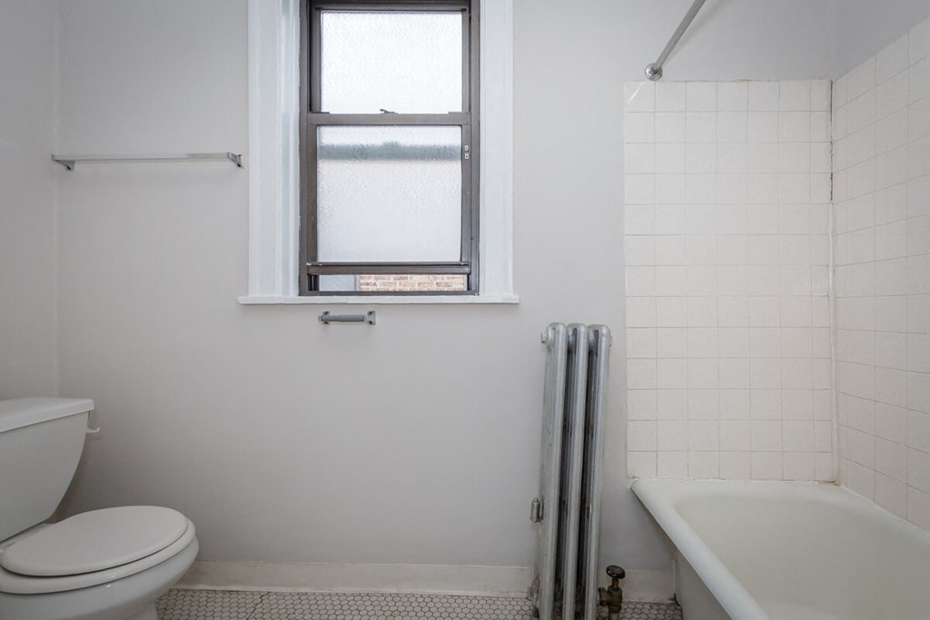 a white bathroom with a window and a toilet and a tub