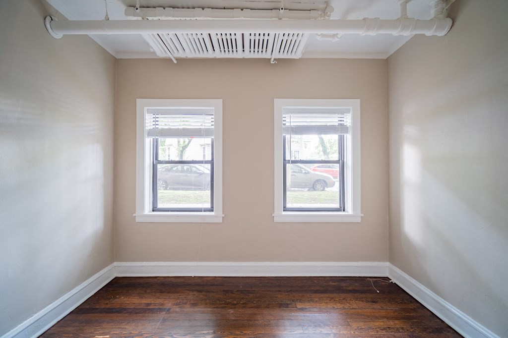 an empty room with two windows and a wood floor