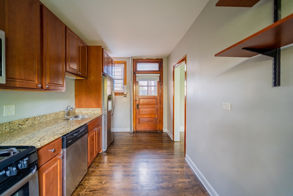 a kitchen with wooden cabinets and granite counter tops and a door to a hallway