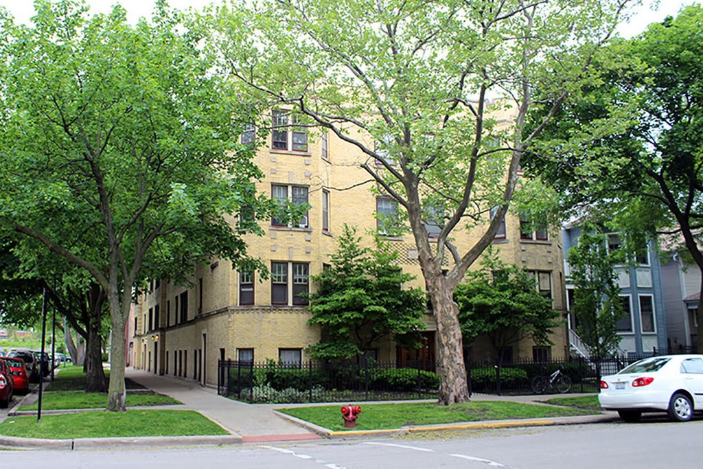 a yellow brick apartment building on a city street with trees