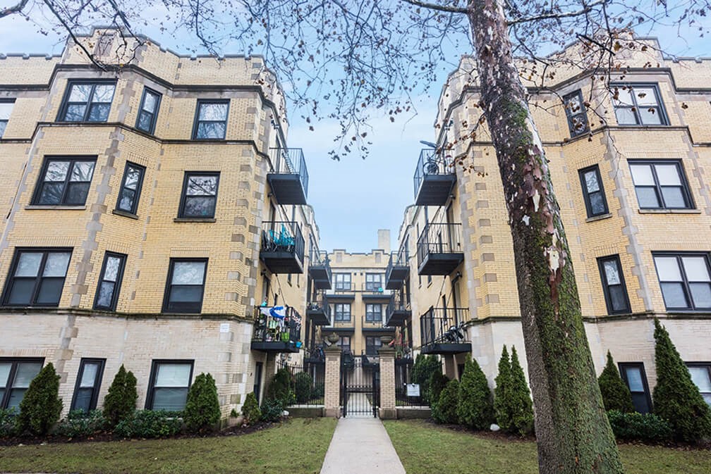 a row of apartments with a sidewalk between them and a tree