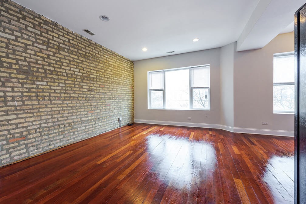 an empty living room with a brick wall and wood floors