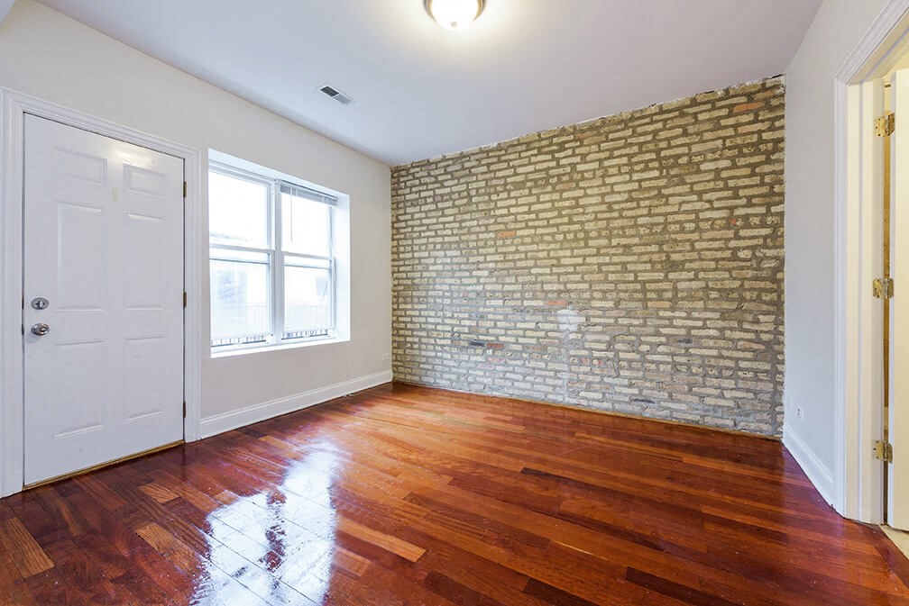 an empty living room with a brick wall and wooden floors