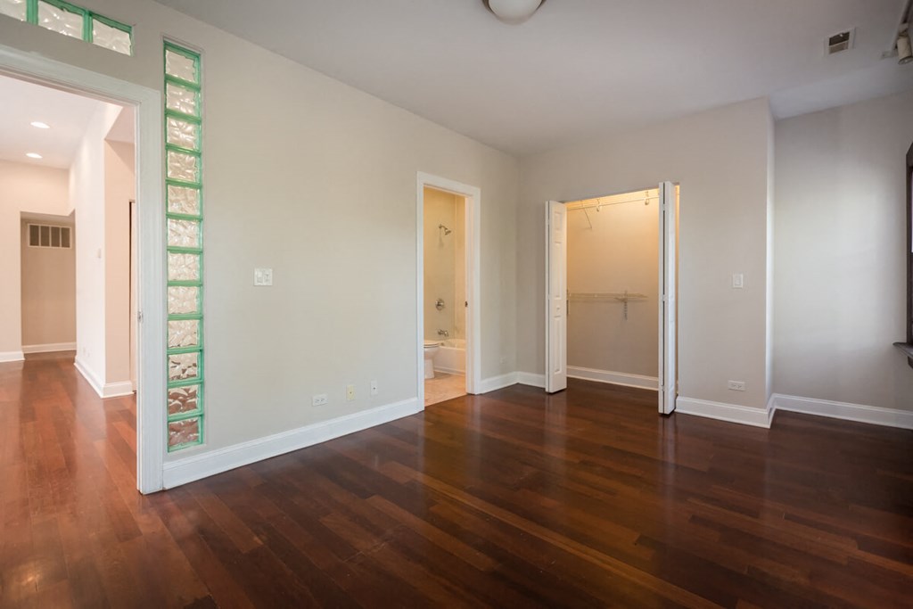 an empty living room with wooden floors and a door to a bathroom