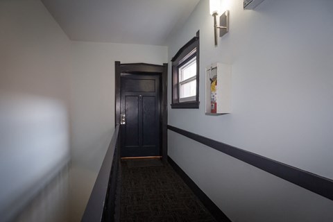 a hallway with white walls and a black door and a window