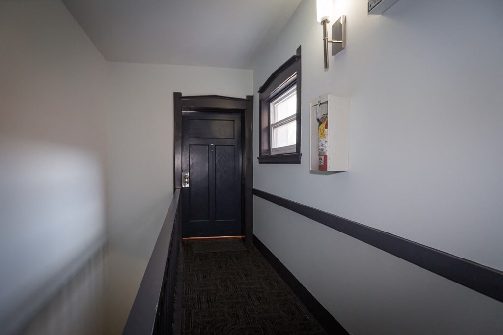 a hallway with white walls and a black door and a window