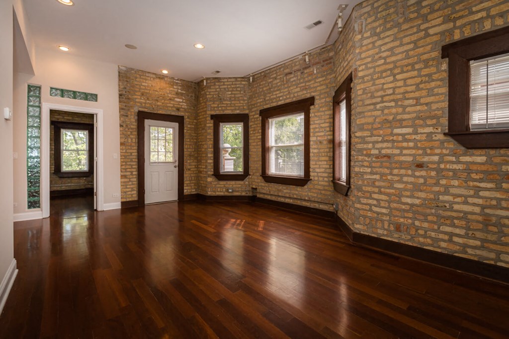 an empty living room with a hard wood floor and brick walls