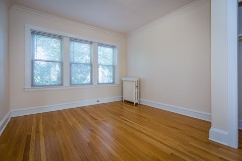 a living room with wood floors and a radiator and three windows