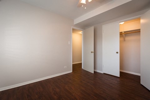 a bedroom with white walls and wood flooring and a closet