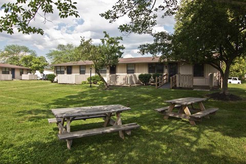two picnic tables in the grass in front of a house