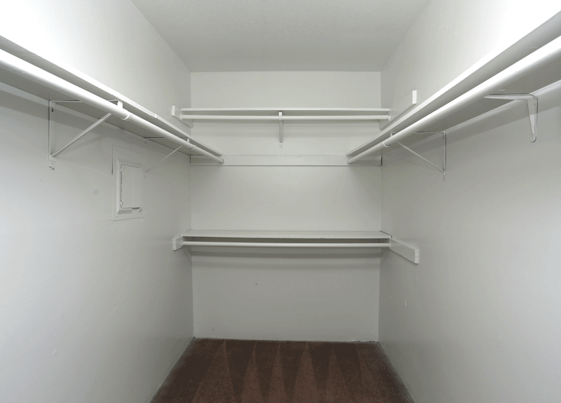 a walk in closet with white walls and a wooden floor