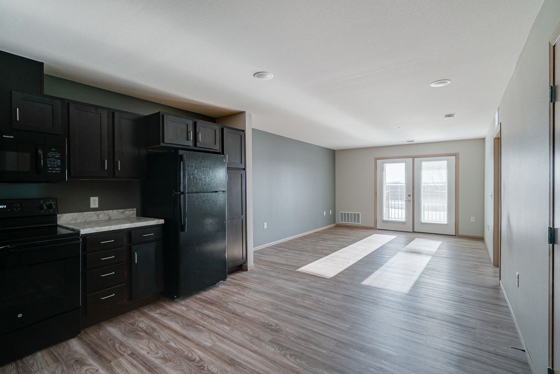 an empty kitchen and living room with black appliances and wood flooring
