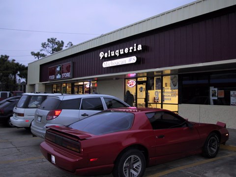 A red car is parked in front of a store called Peluqueria.