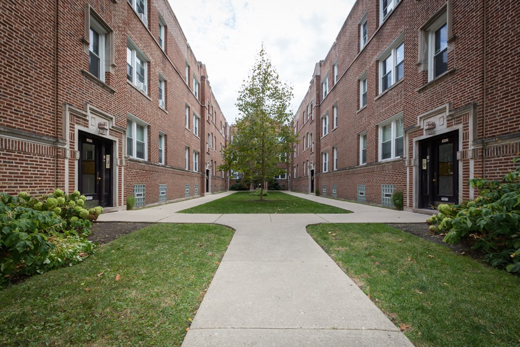 a walkway between two brick apartment buildings with grass and trees