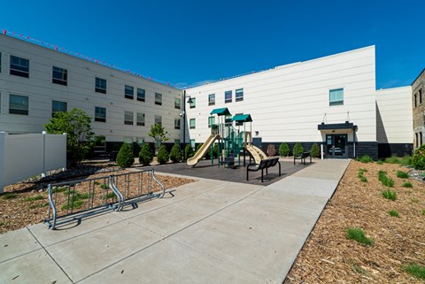 A playground area in front of a white building with a slide and a climbing frame.