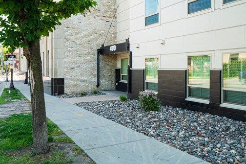A white building with a black awning and a tree in front of it.