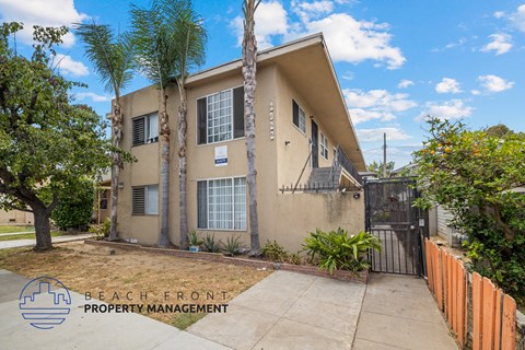 a beige house with palm trees and a sidewalk in front of it