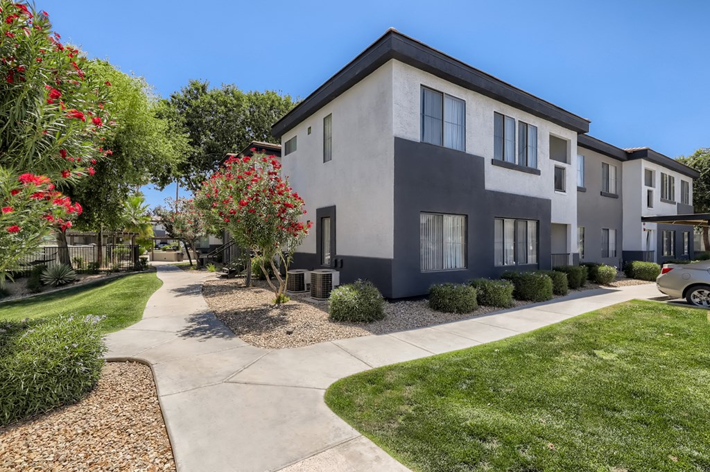 an apartment building with a sidewalk and trees in front of it