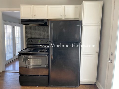 A black fridge and stove in a kitchen with white cabinets.