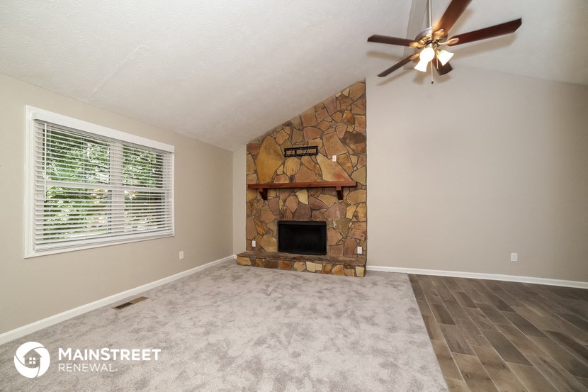 the living room with a stone fireplace and a ceiling fan