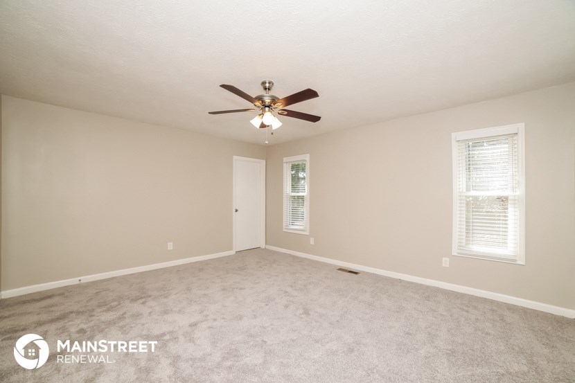 the spacious living room with ceiling fan and carpeting