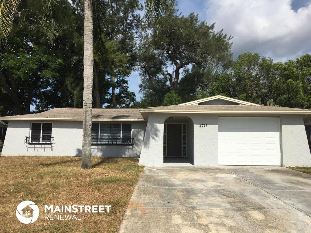 a white house with a garage door and a palm tree
