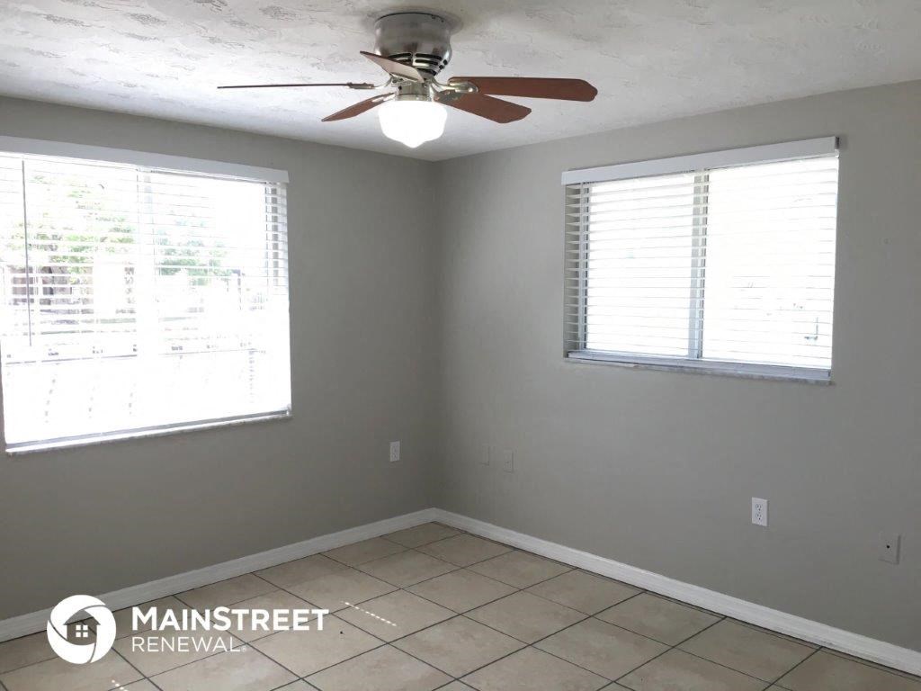 an empty room with a ceiling fan and two windows