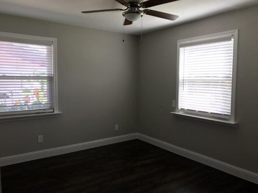 an empty room with a ceiling fan and two windows