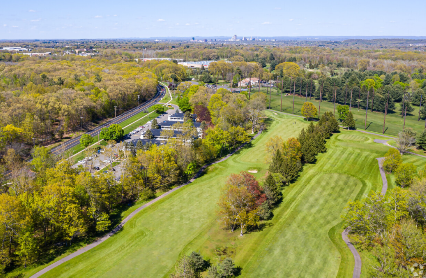 an aerial view of a golf course with trees and a highway