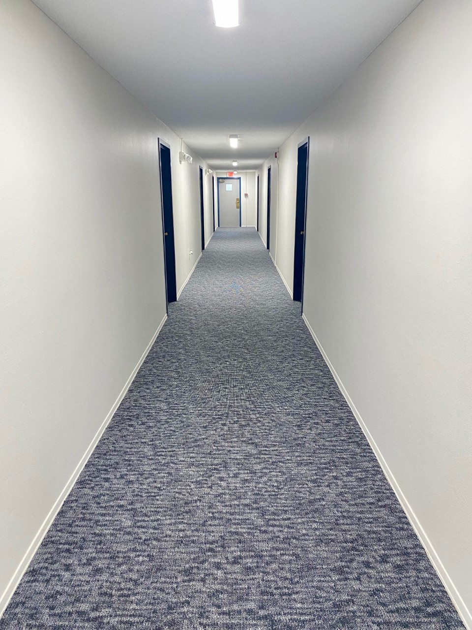 a long hallway with white walls and blue carpeting and white doors
