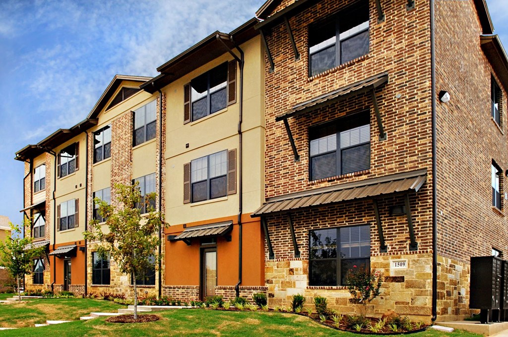 A brick building with a green lawn in front at Centre Place Apartments, Denton, TX