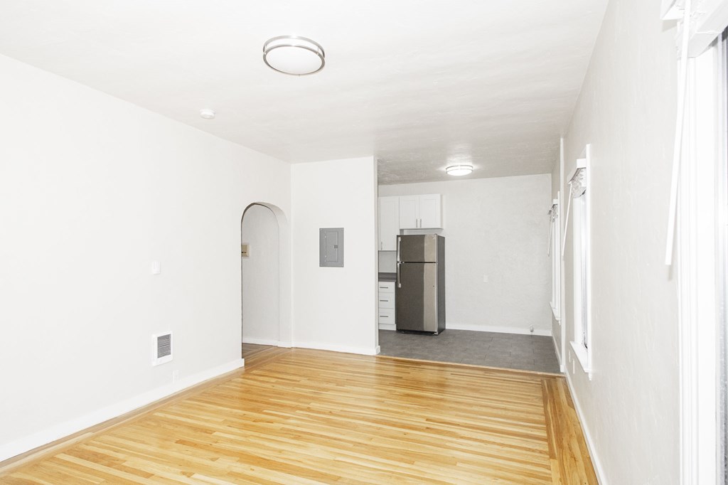 A kitchen area with a refrigerator and a wooden floor.