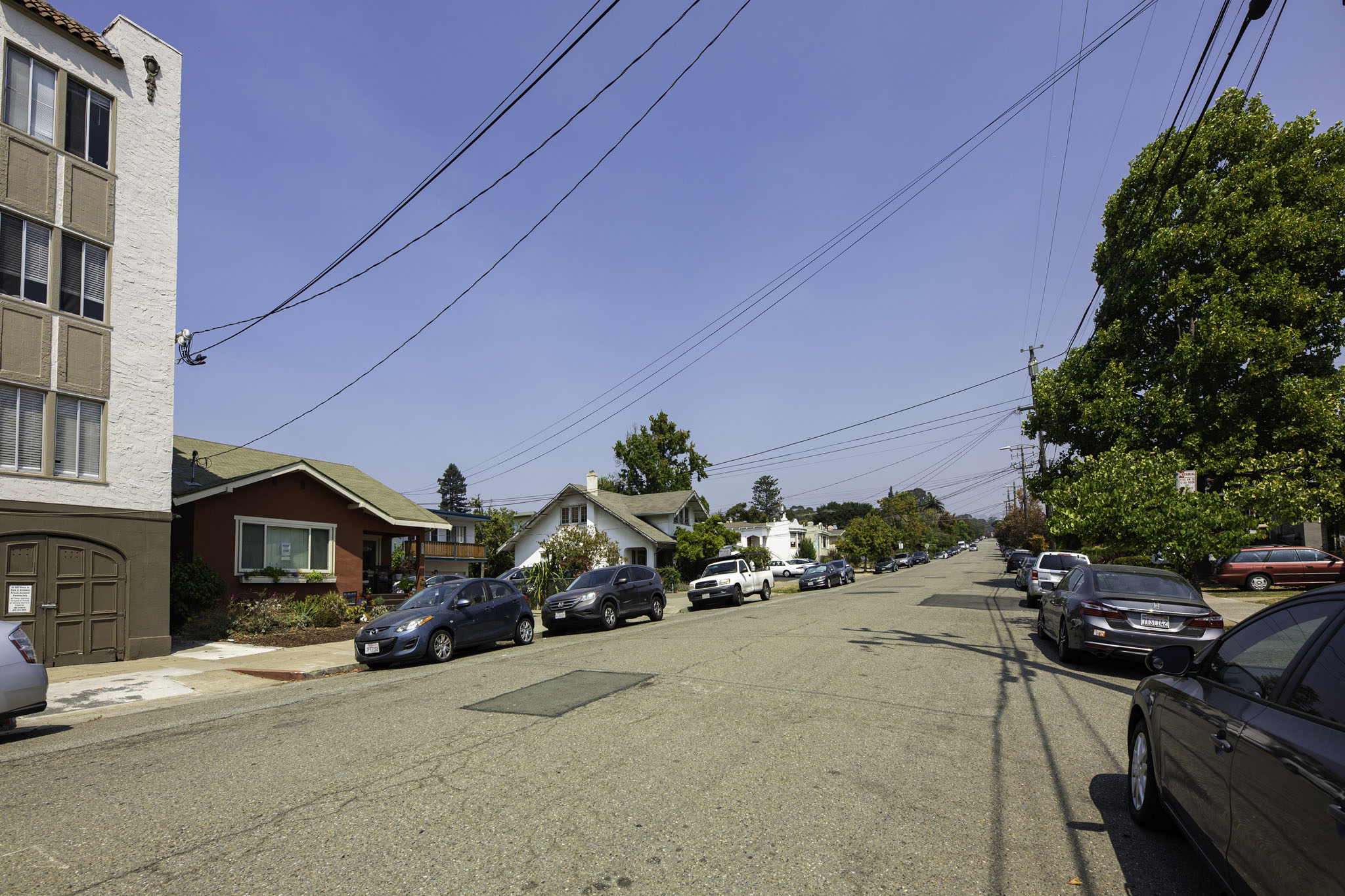 A street with cars parked on both sides and houses in the background.