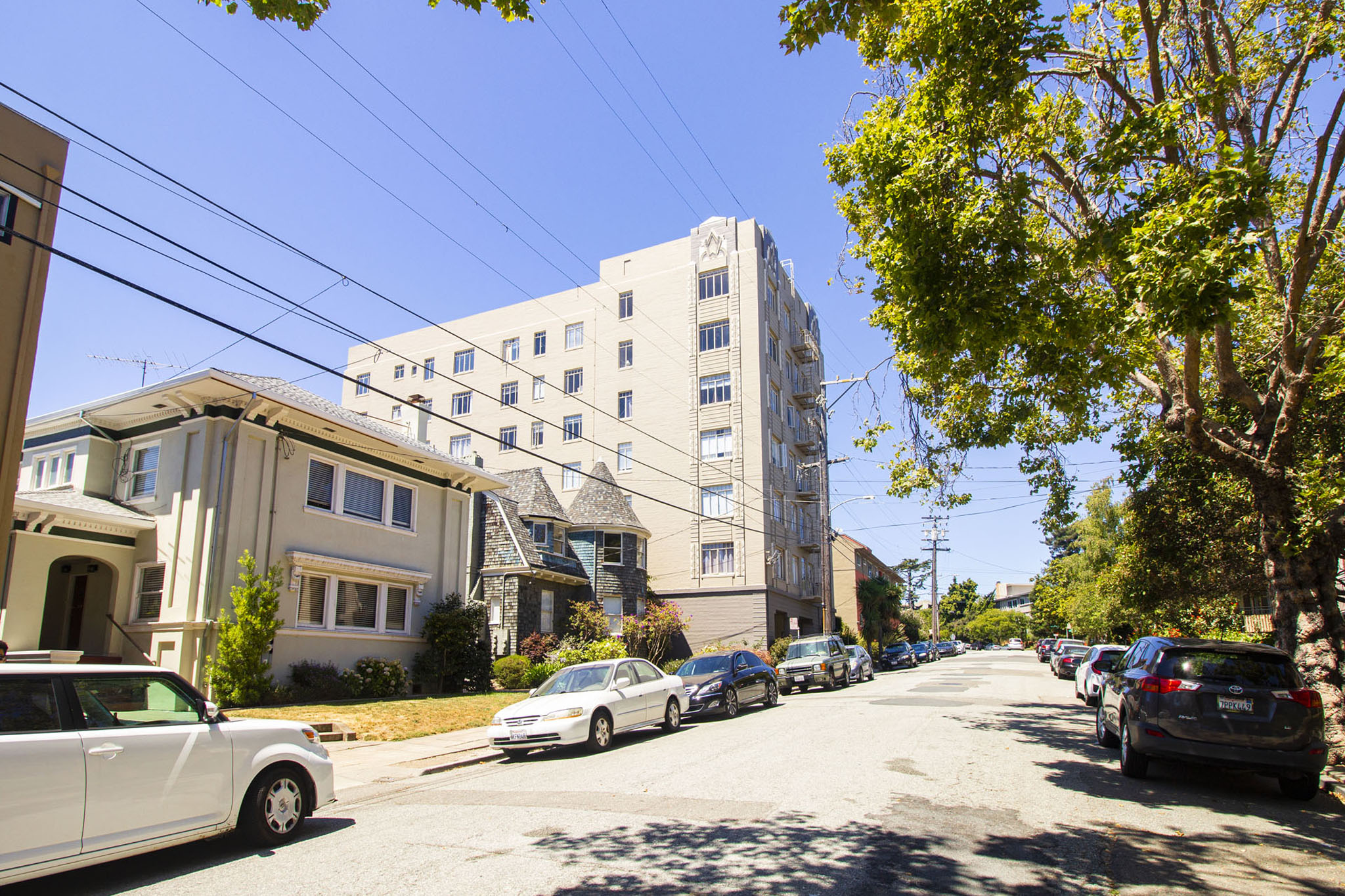 A street view with cars parked on the side and apartment buildings in the background.