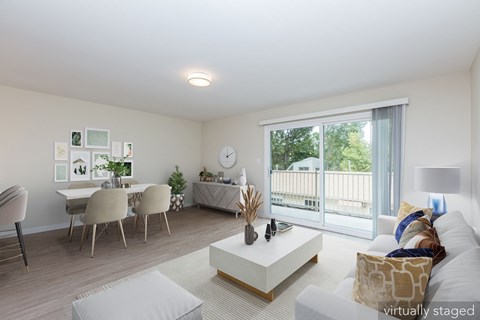 A living room with a white couch, a coffee table, a dining table with chairs, and a balcony with a view of the outdoors.