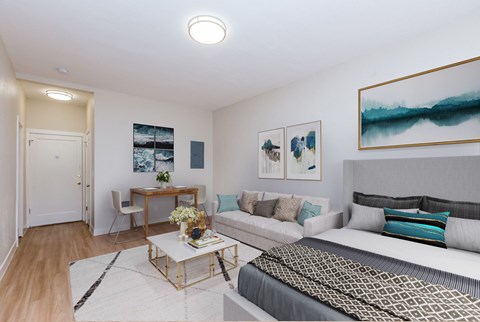 A well-lit bedroom with a bed, couch, and artwork on the walls.