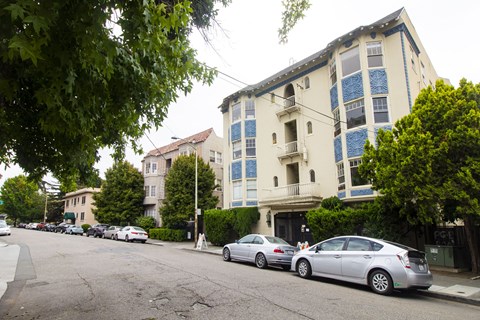A street with cars parked on the side and apartment buildings in the background.