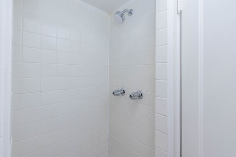 A white tiled shower with a door on the right.