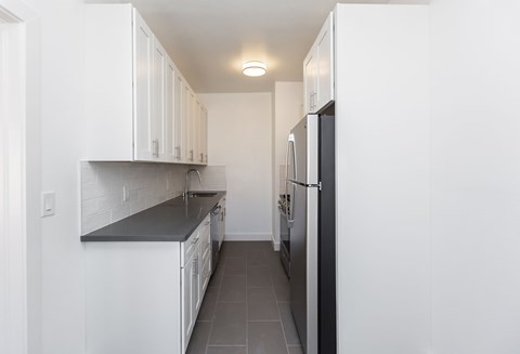 A kitchen with white cabinets and a black fridge.