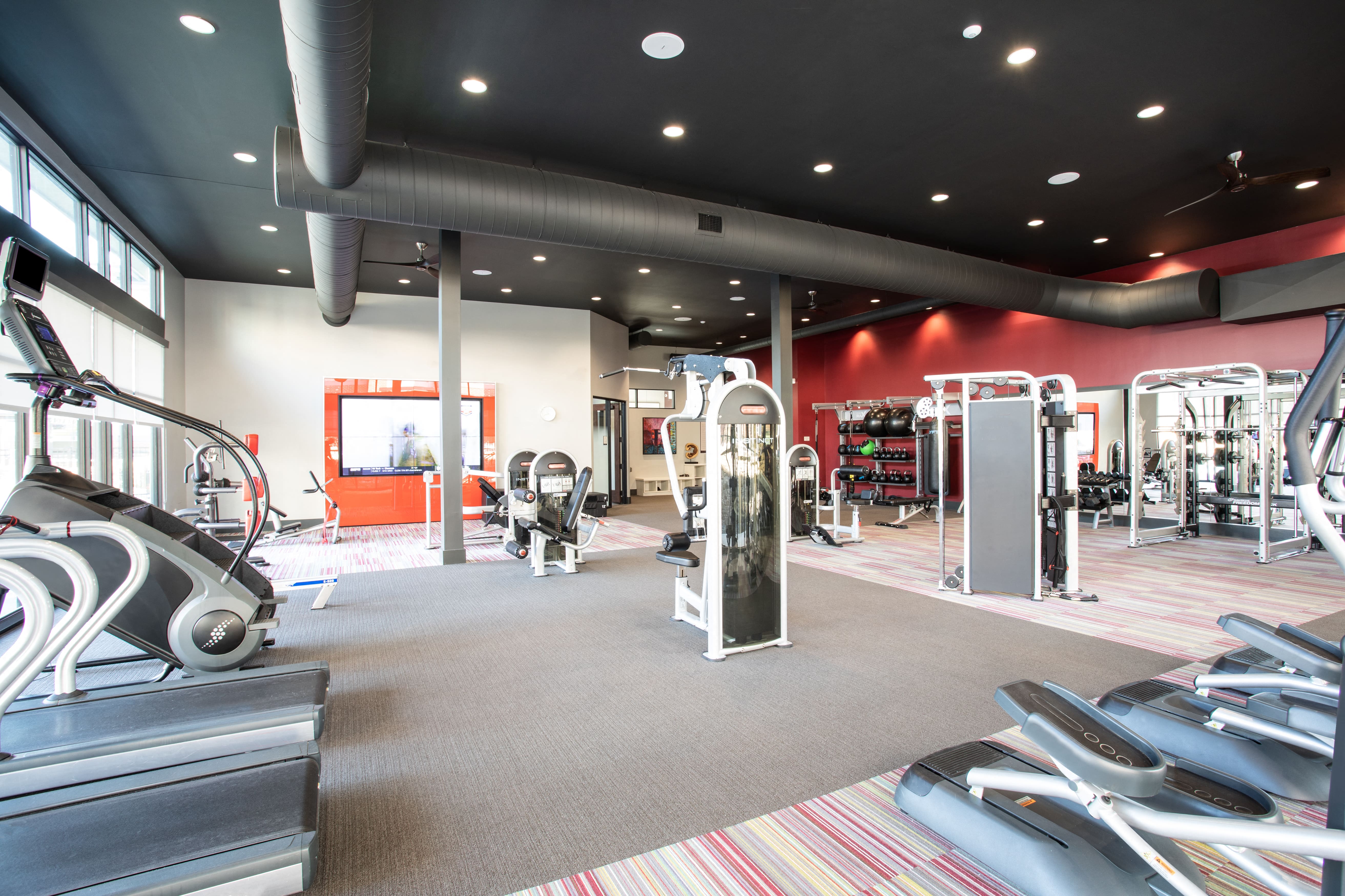 a gym with cardio machines and weights on the floor and a tv on the wall